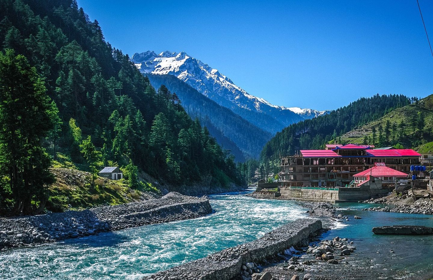 The Swat River at Kalam, with a red-roofed hotel and snowy peaks beyond