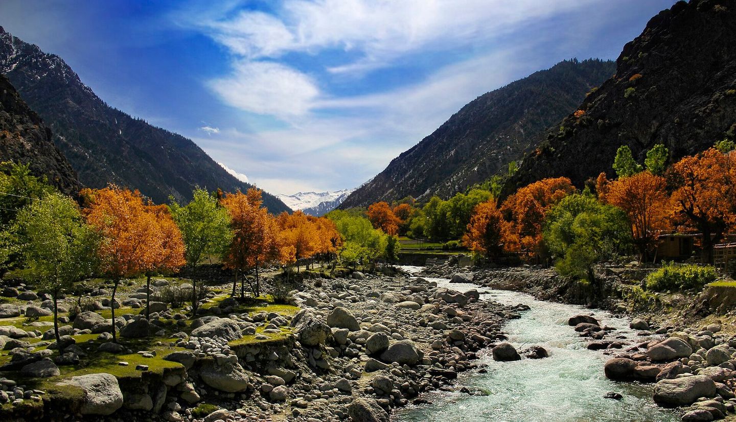 The Bumburet river running over boulders between autumn trees