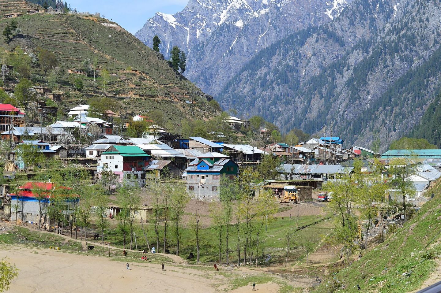 The houses of Arang Kel on a green hillside, with snowy mountains behind