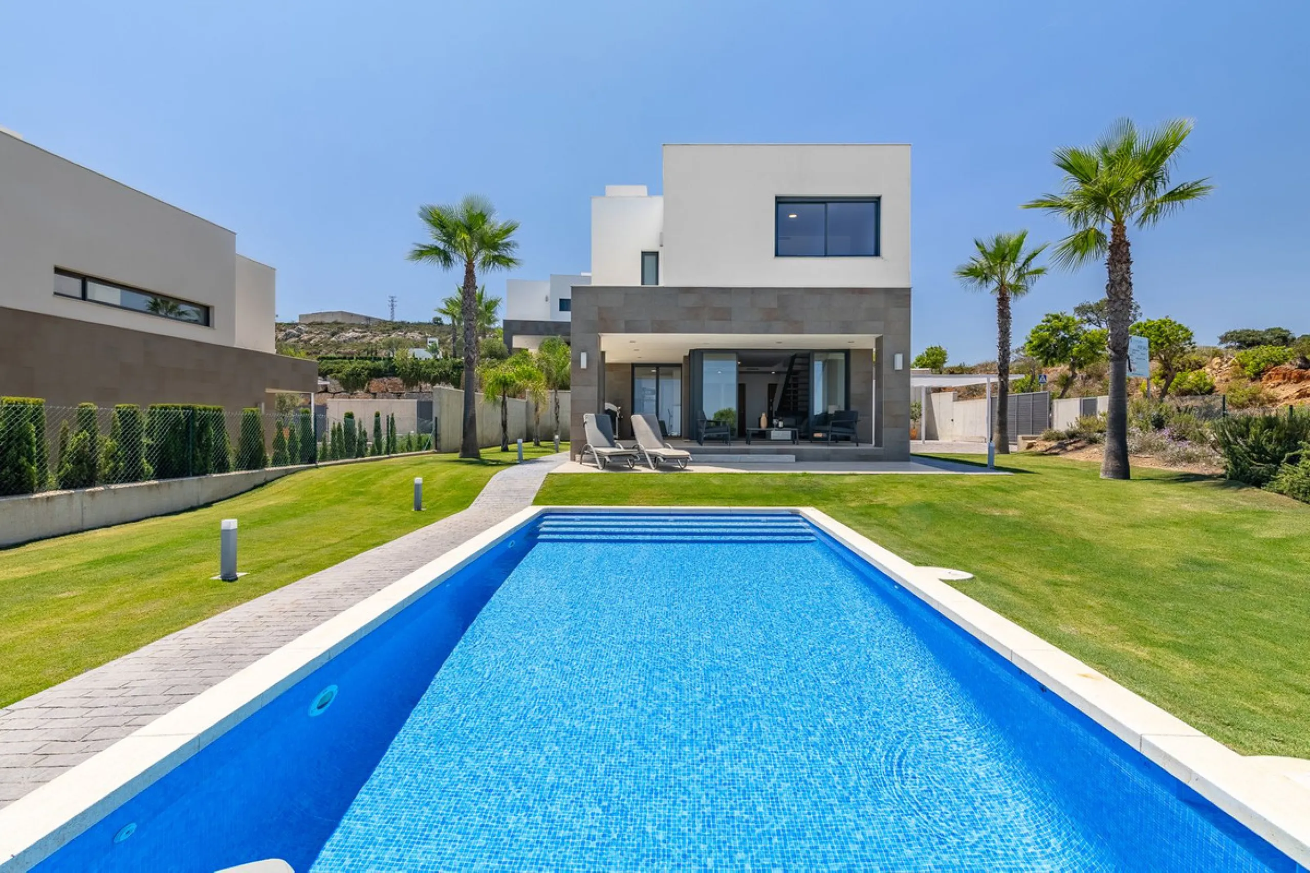 This stunning two-story villa boasts four spacious bedrooms, each with fitted wardrobes, electric blinds, and individual air conditioning control. The three elegant bathrooms feature the comfort of underfloor heating.