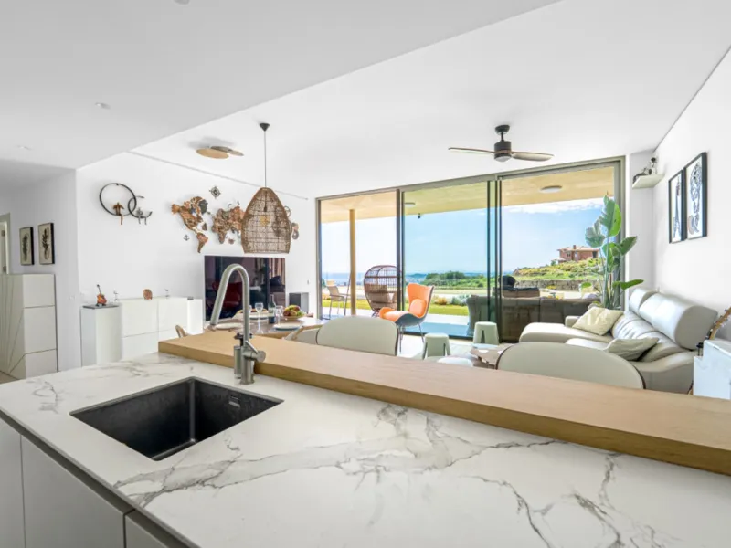 Apartment West is a ground-floor luxury home with uninterrupted sea views that stretch across the horizon. The open-plan living area is filled with natural light through floor-to-ceiling terrace doors. The kitchen features marble countertops, sleek neutra