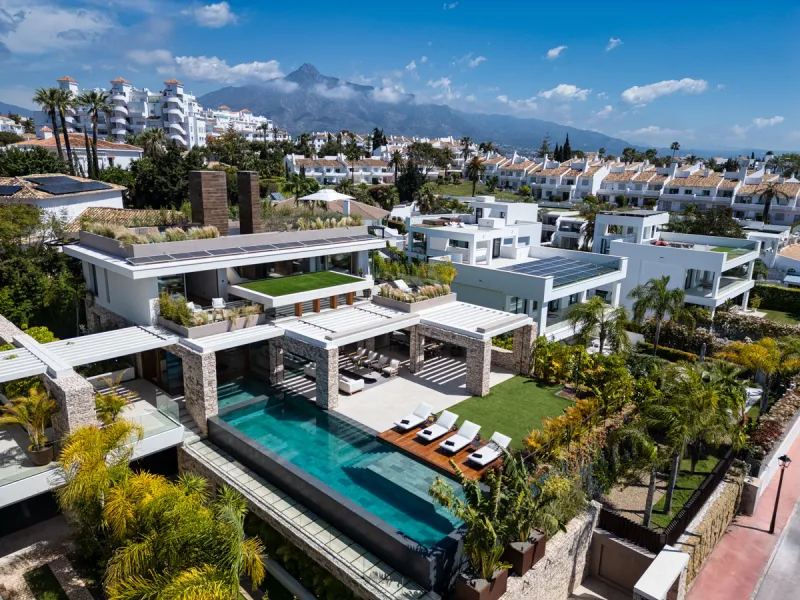 Nestled gracefully upon the verdant slopes of Nueva Andalucía, this villa is a triumph of modern elegance and luxurious design, an embodiment of serene sophistication. As you approach the property, you are greeted by a grand entrance framed by sleek lines
