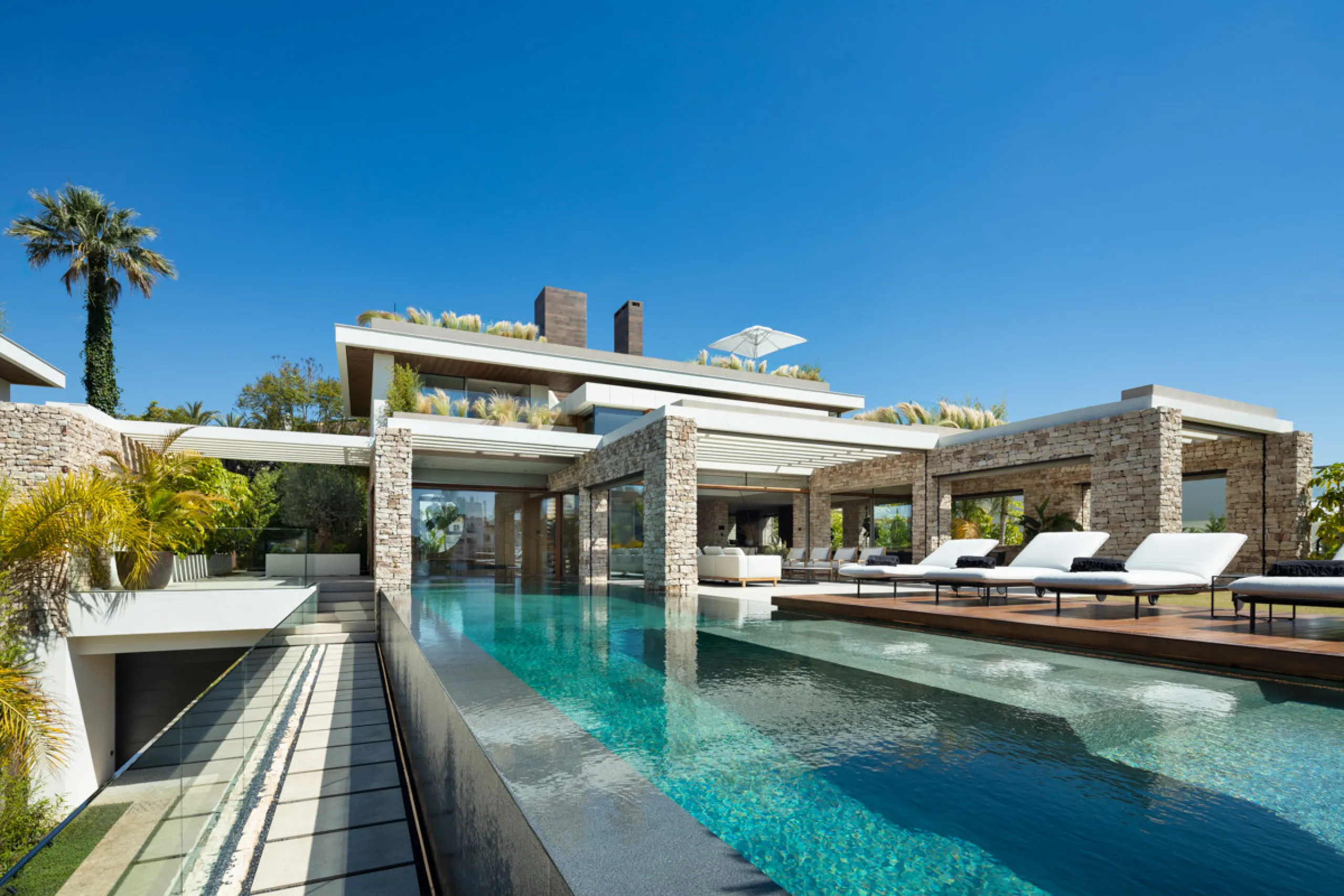 Nestled gracefully upon the verdant slopes of Nueva Andalucía, this villa is a triumph of modern elegance and luxurious design, an embodiment of serene sophistication. As you approach the property, you are greeted by a grand entrance framed by sleek lines