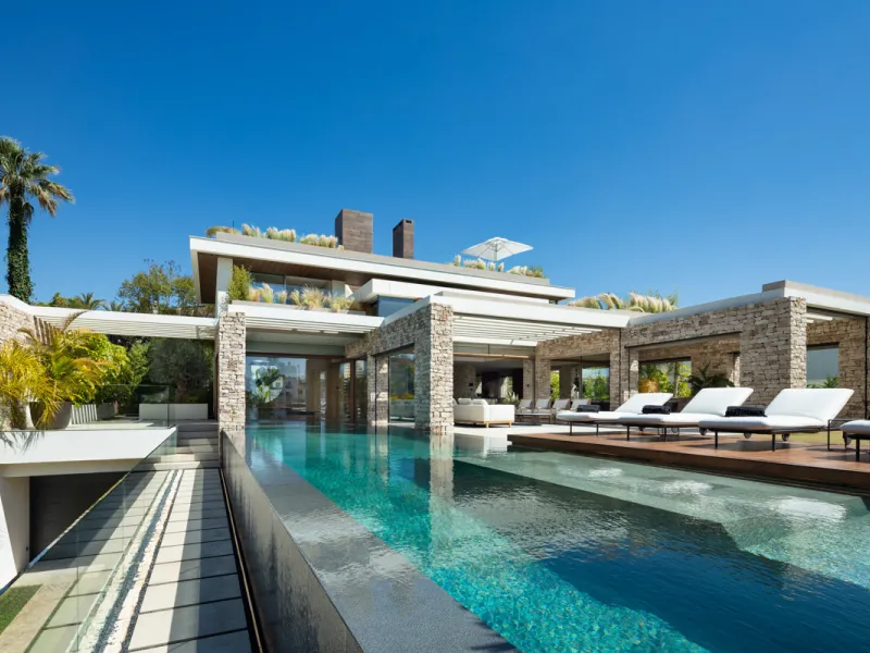 Nestled gracefully upon the verdant slopes of Nueva Andalucía, this villa is a triumph of modern elegance and luxurious design, an embodiment of serene sophistication. As you approach the property, you are greeted by a grand entrance framed by sleek lines