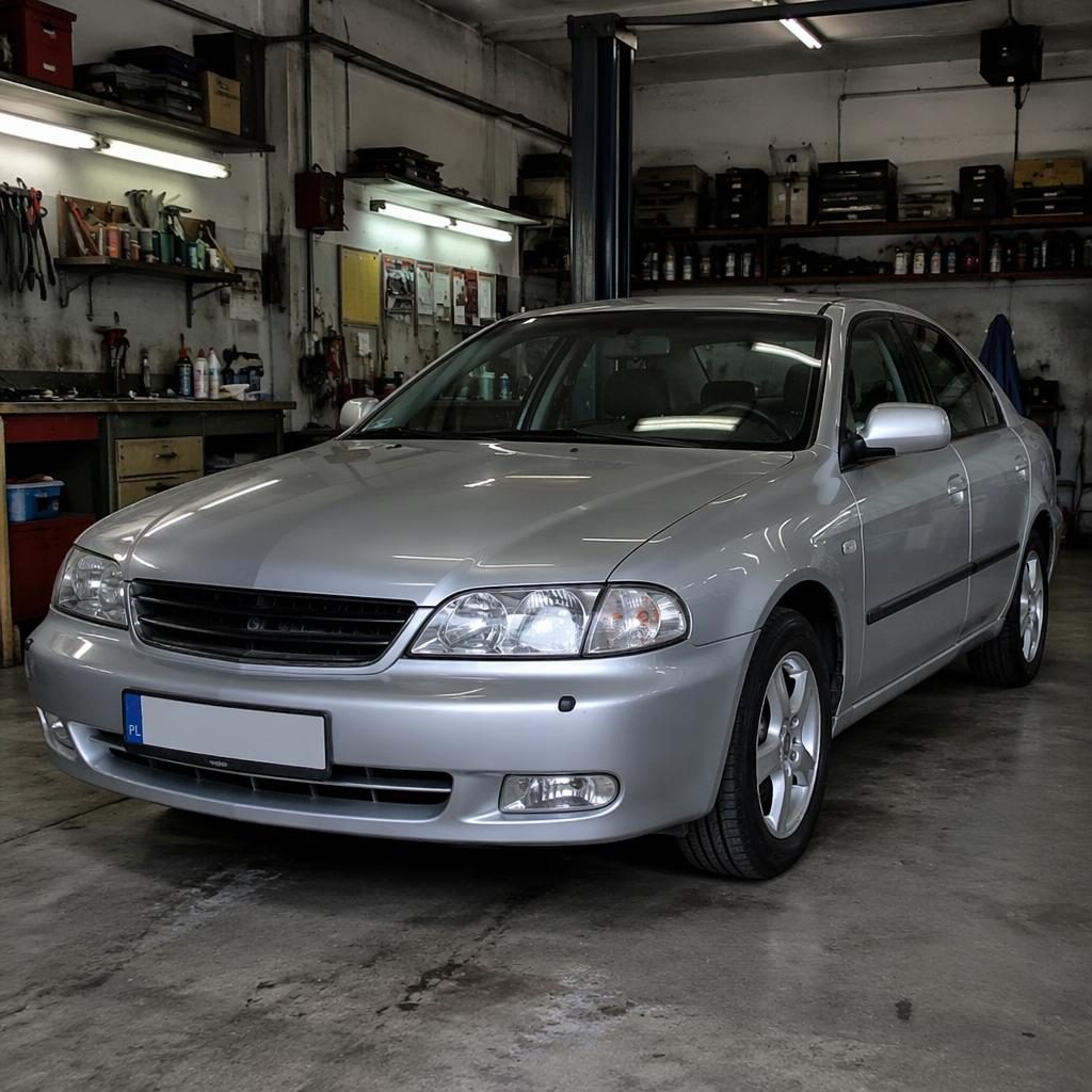 Srebrny sedan z lat 2000, ujęcie 3/4 z przodu, stoi w garażu warsztatowym w realistycznej scenie sprzedaży auta.
