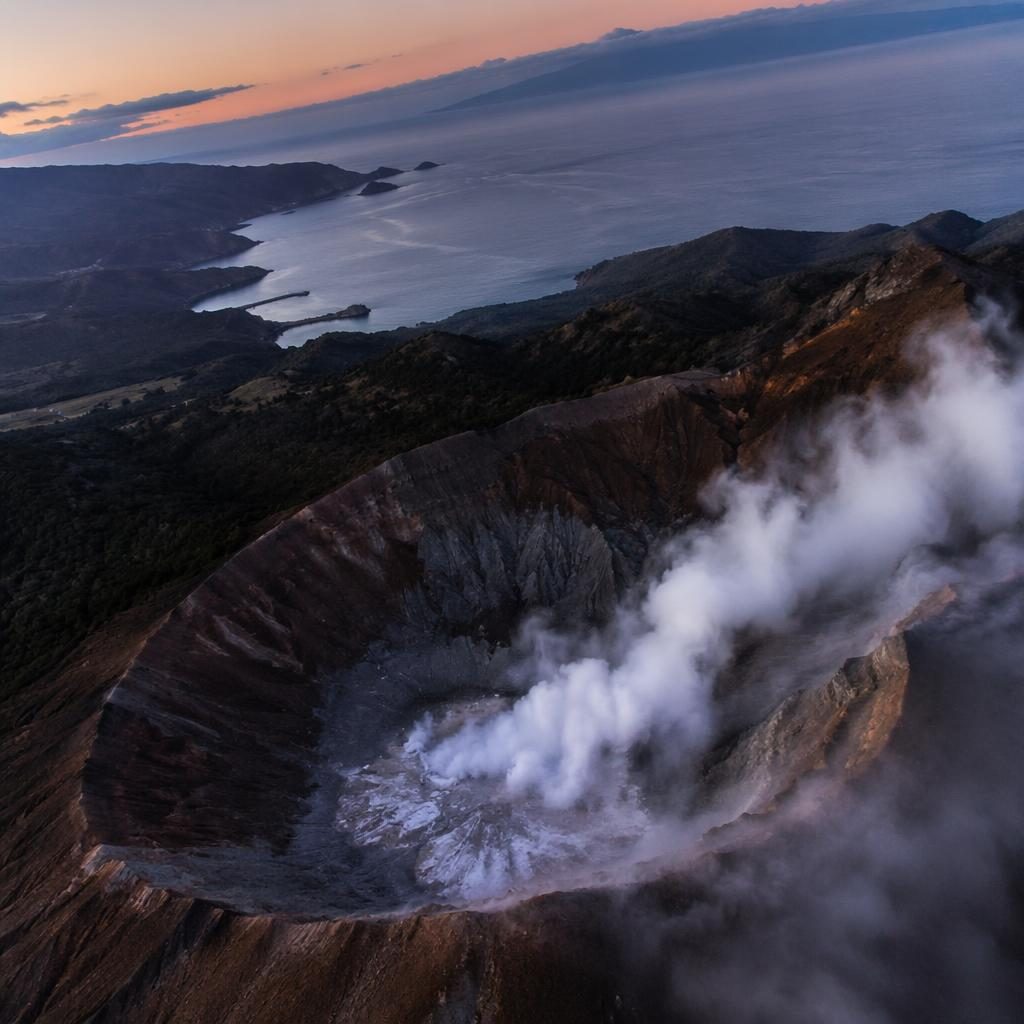 Drone aerial view of wine country at dusk, tilted top-down over vineyards near a steaming volcanic crater