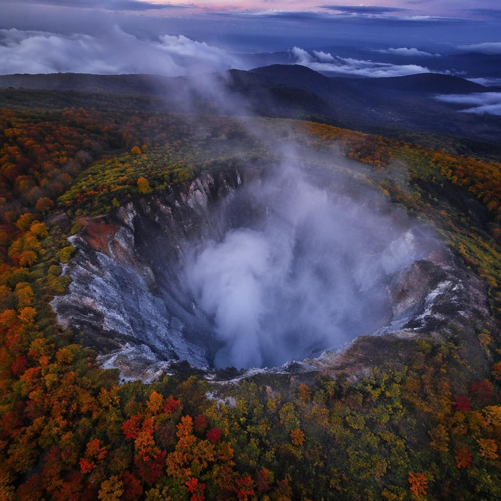 Drone aerial view of an autumn forest canopy at blue hour with volcanic crater steam rising in vibrant natural tones.