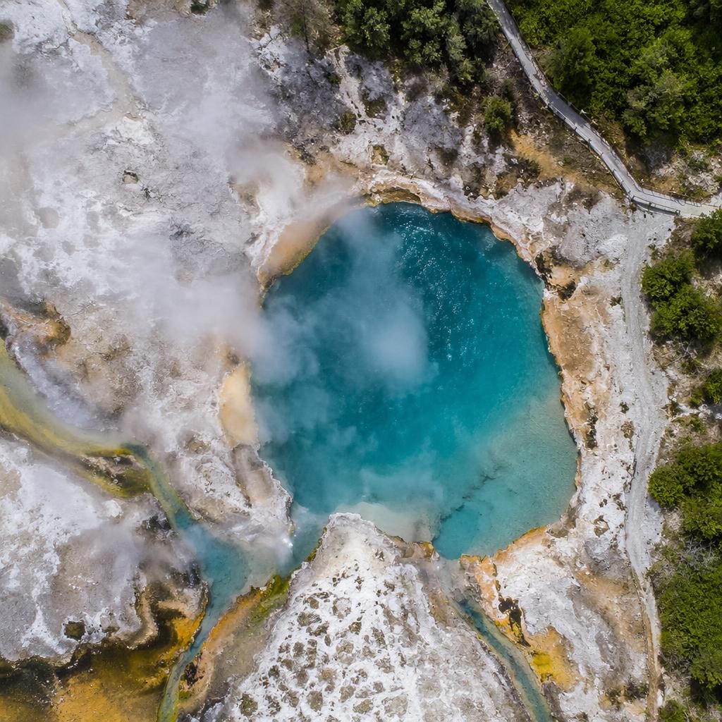 Drone aerial view of New Zealand thermal hot springs at noon with vivid mineral pools, steam, and sharp top-down detail.