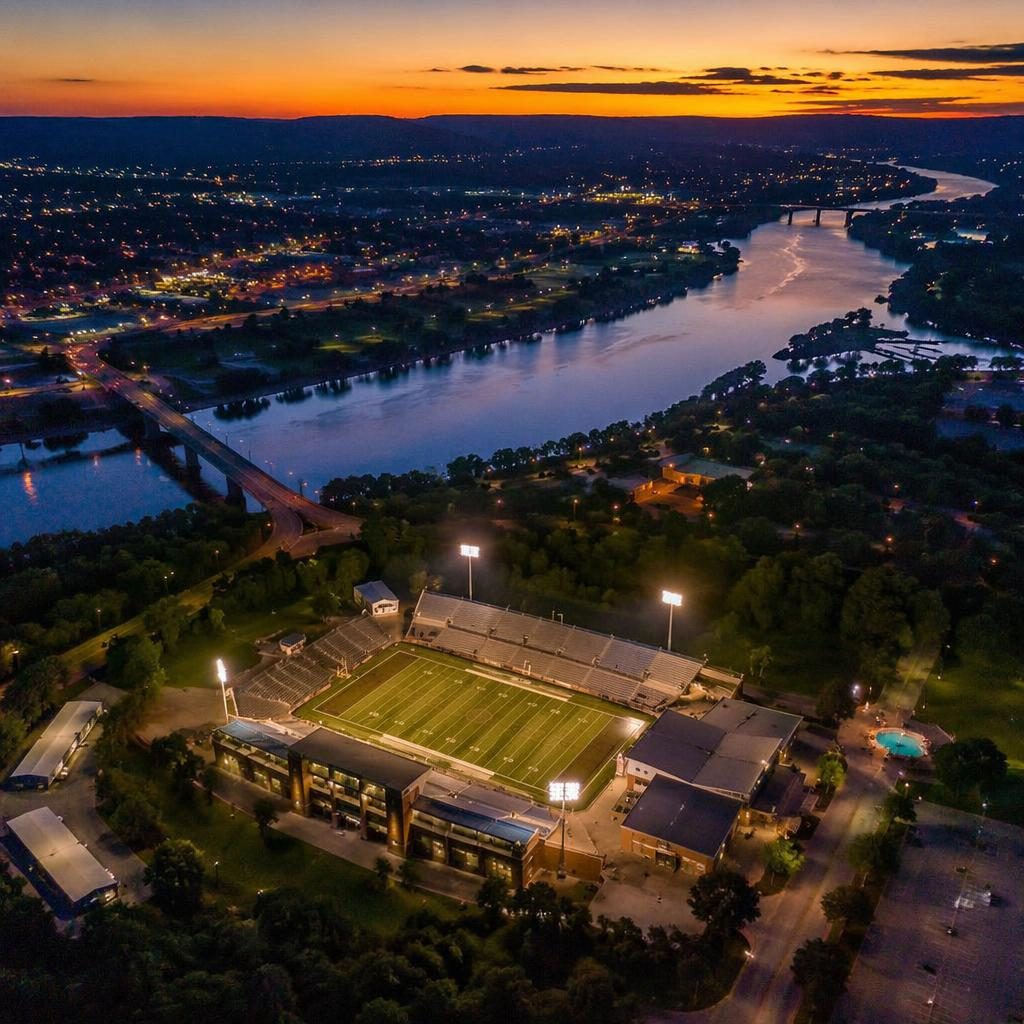Top-down drone aerial of a river winding through a valley at night, city lights glowing, cool blue tones, panoramic view.