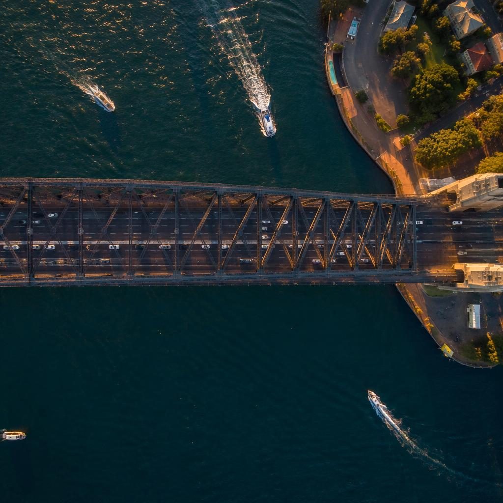 Top-down drone view of Sydney Harbour Bridge at golden hour with warm light, sharp structural detail, and surrounding water