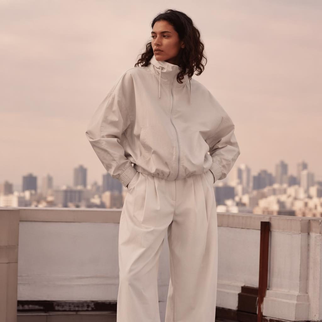 Editorial fashion model in pastel athletic-inspired outfit on a rooftop city setting with soft luxury styling