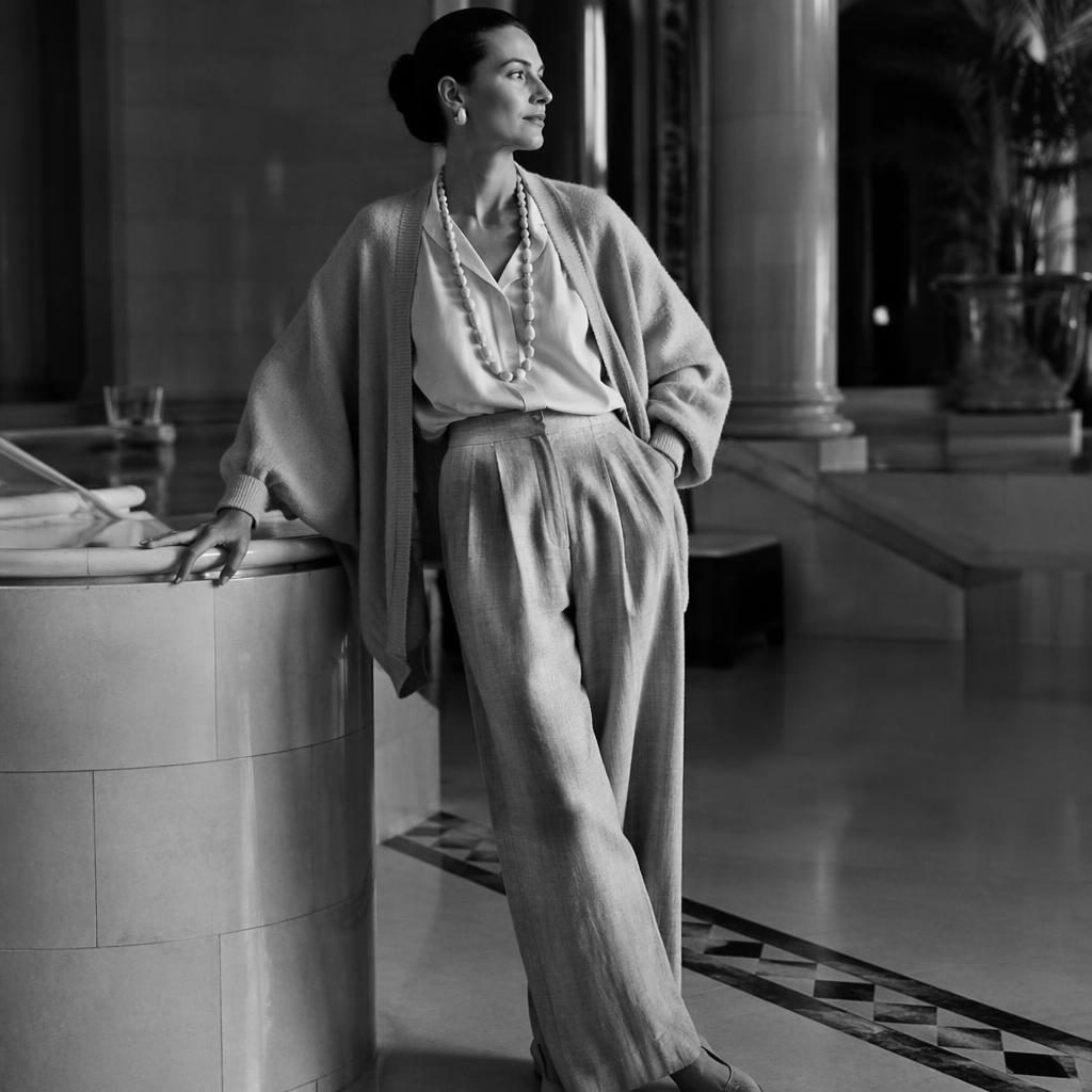 Editorial fashion model in a luxury hotel lobby wearing a coastal grandmother look in cool gray tones, posed naturally.