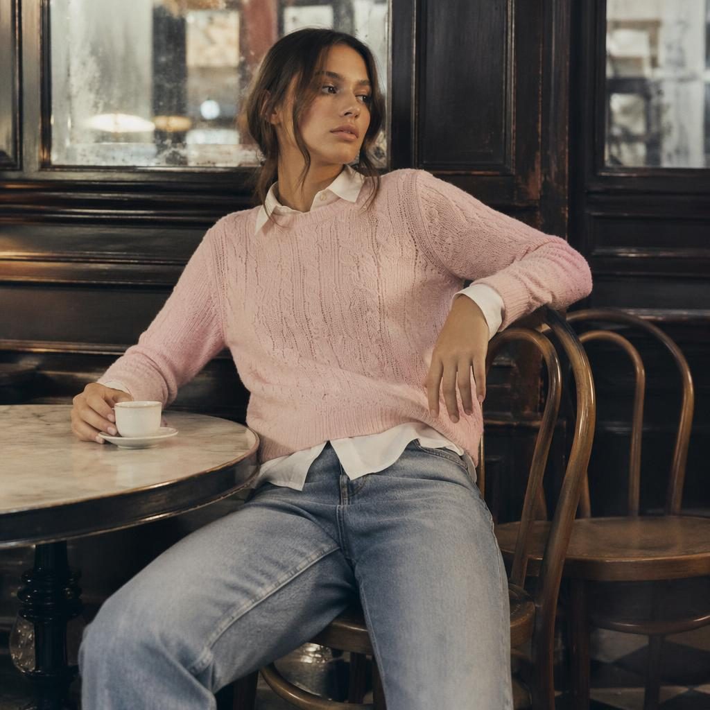 Editorial fashion model in a marco polo lookbook outfit posing naturally inside a vintage cafe with dark moody light