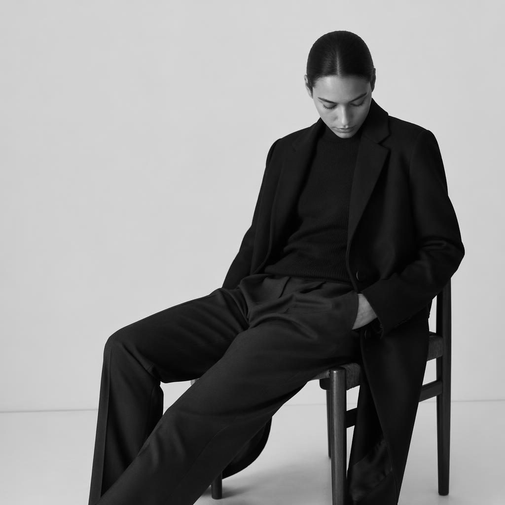 Black and white editorial fashion lookbook photo of a generic model in a minimalist white space with a quiet natural pose.