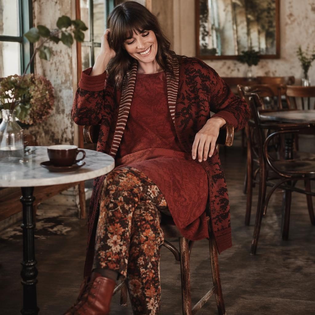 Editorial fashion model in a minimalist autumn outfit posed candidly inside a vintage cafe with warm rust tones