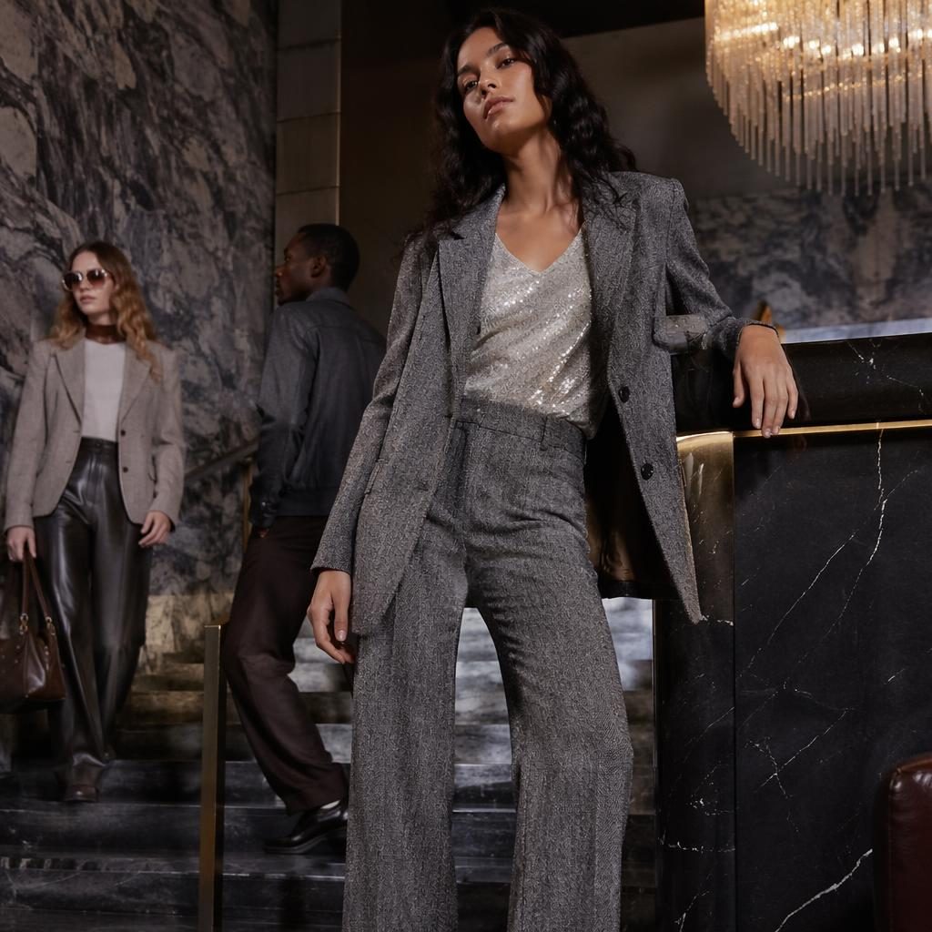Model in an H&M lookbook outfit posing naturally in a luxury hotel lobby with a vintage 70s style and cool gray tones.