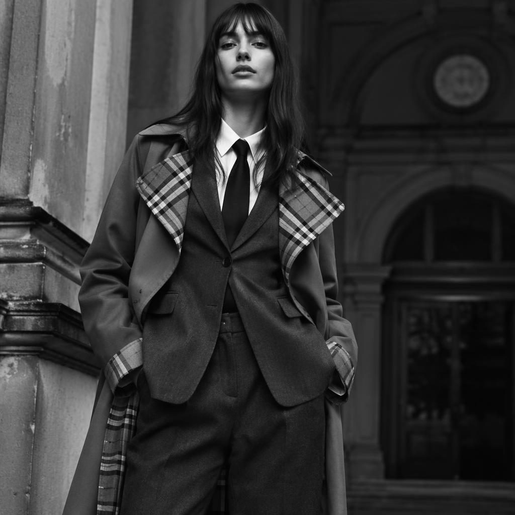 Black and white editorial fashion photo of a model in a Burberry-inspired look outside an architectural building
