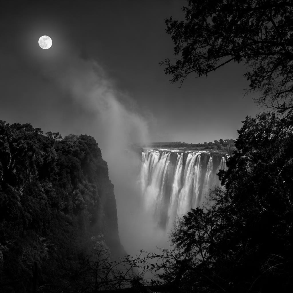 Schwarzweiß-Naturfoto eines Herbstwalds bei Vollmond mit Nebel und rauchender Gischt an den Victoriafällen