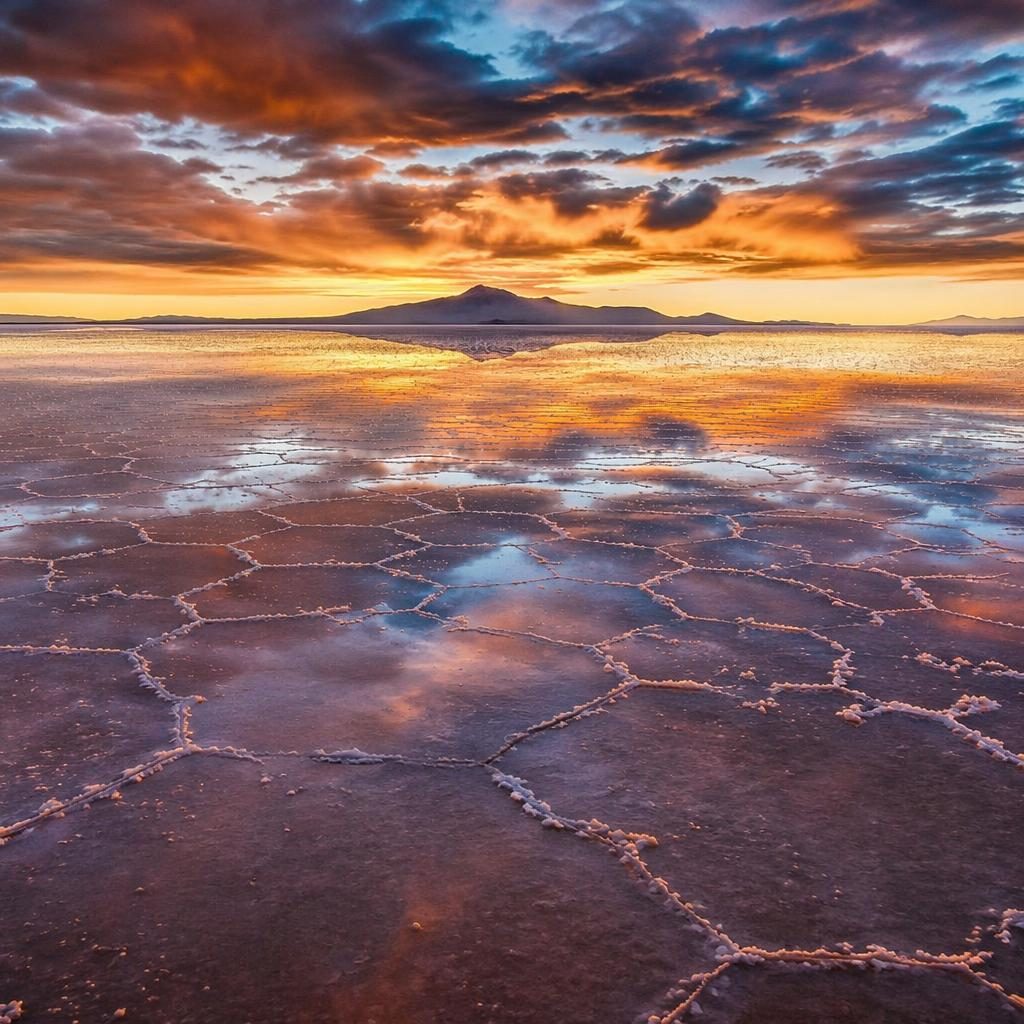 Spiegelnde Salzfläche in Bolivien unter bewölktem Himmel, mit herbstlich warmen Farbtönen und dramatischem Licht