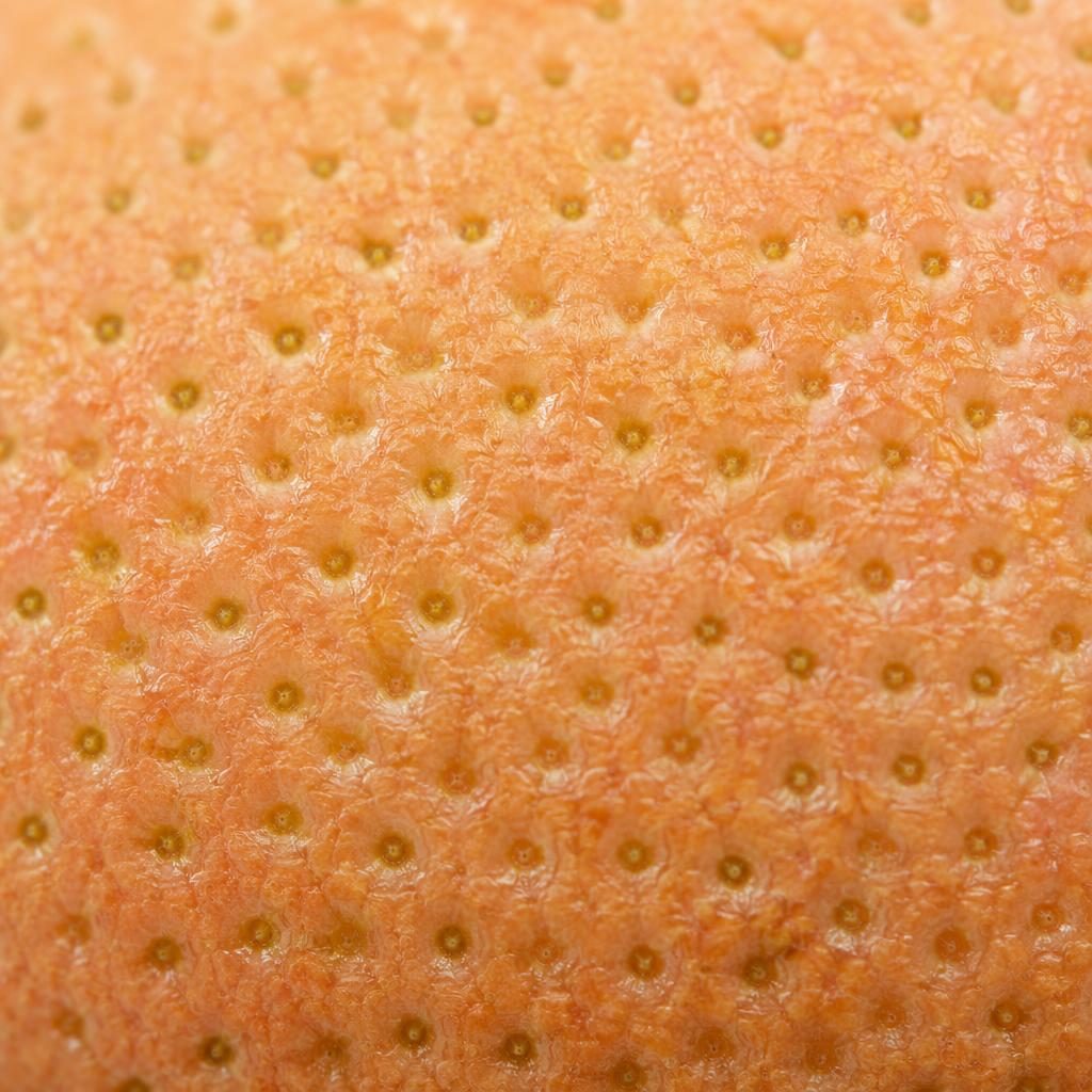 Macro close-up of fruit peel pores under ring light, shown with extreme detail, soft pastel tones, and full focus.