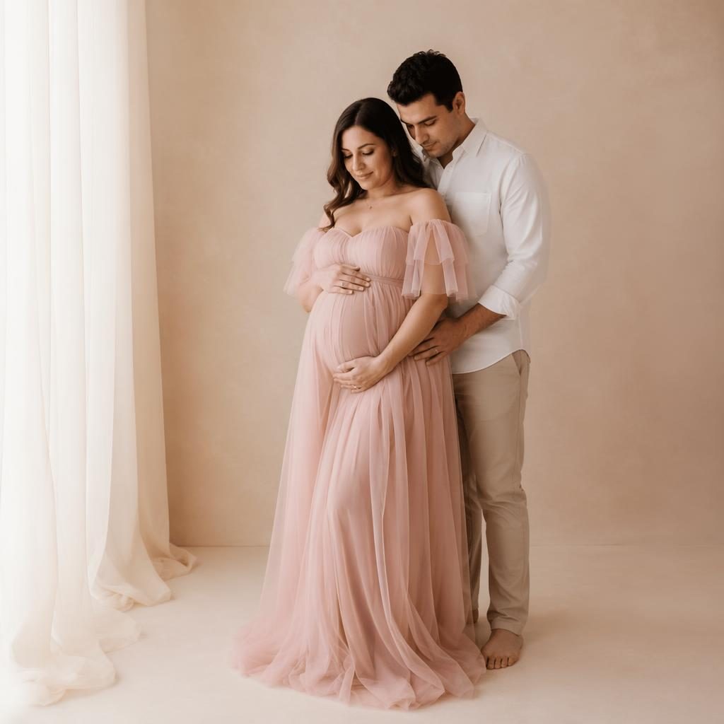 Pregnant woman and partner pose closely in a soft-lit studio, full-body framing, warm cream and rose tones.