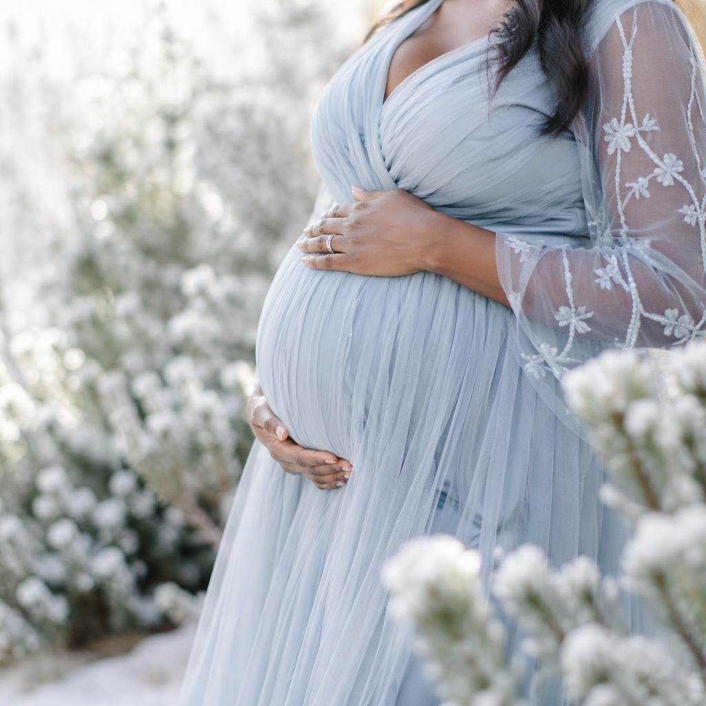 Close-up maternity outdoor portrait of a pregnant belly in a botanical garden with soft pastel tones and editorial light.