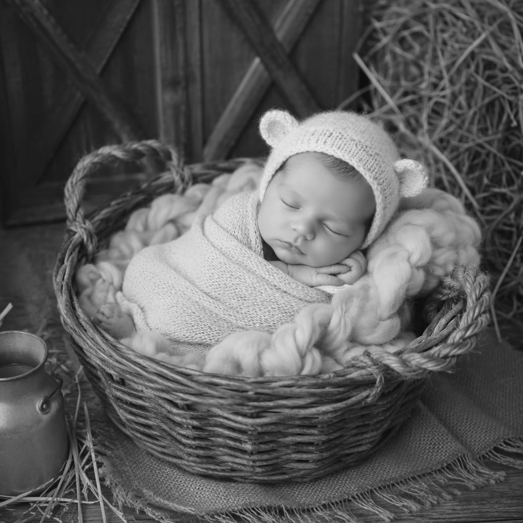 Nouveau-né endormi, emmailloté dans un panier rustique tressé, photo studio noir et blanc à lumière douce.