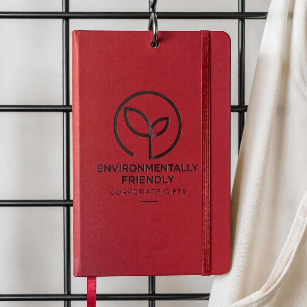 Photo-real red notebook mockup hanging on a rack with a large generic logo in a minimal monochrome studio setup.