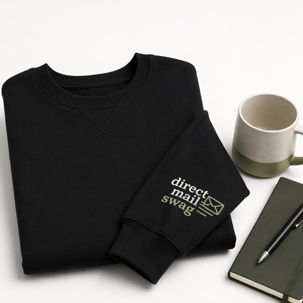 Black crewneck sweatshirt mockup on a white background with a sage and ivory direct mail swag logo on the sleeve.