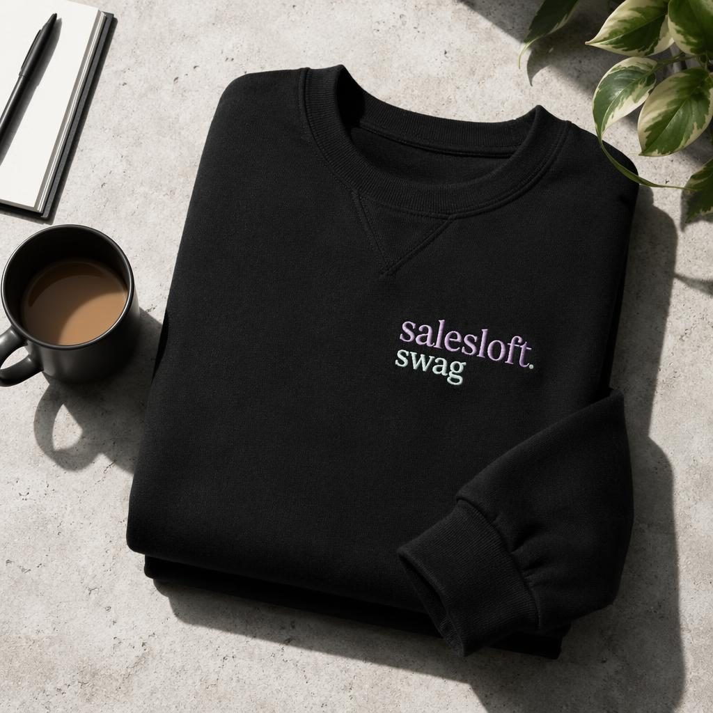 Studio flat lay of a black sweatshirt mockup with salesloft swag embroidery in a soft pastel palette
