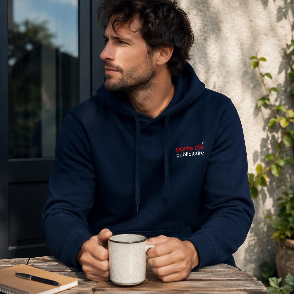 Hoodie bleu marine en photo lifestyle extérieur, avec petit logo rouge et blanc porte clé publicitaire sur la poitrine