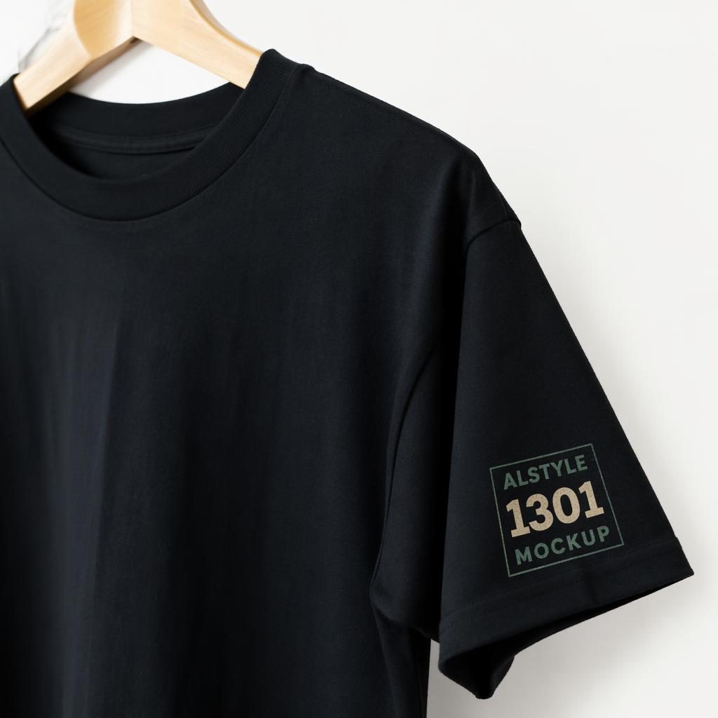 Black t-shirt product mockup on a white background with a small sage and ivory sleeve logo, shown in sharp studio lighting.
