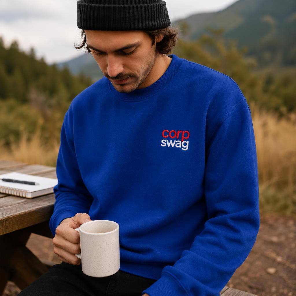 Photo-real royal blue sweatshirt mockup outdoors with red and white corp swag embroidered logo and natural fabric texture.