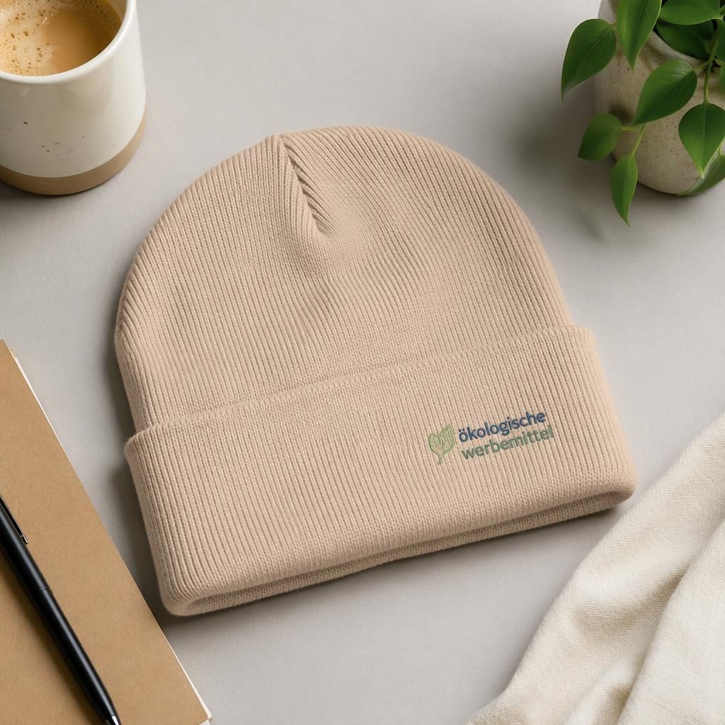 Sandbeige Beanie als Studio Flat Lay mit kleinem Logo ökologische werbemittel, scharfe Stoffstruktur, pastellige Farben.