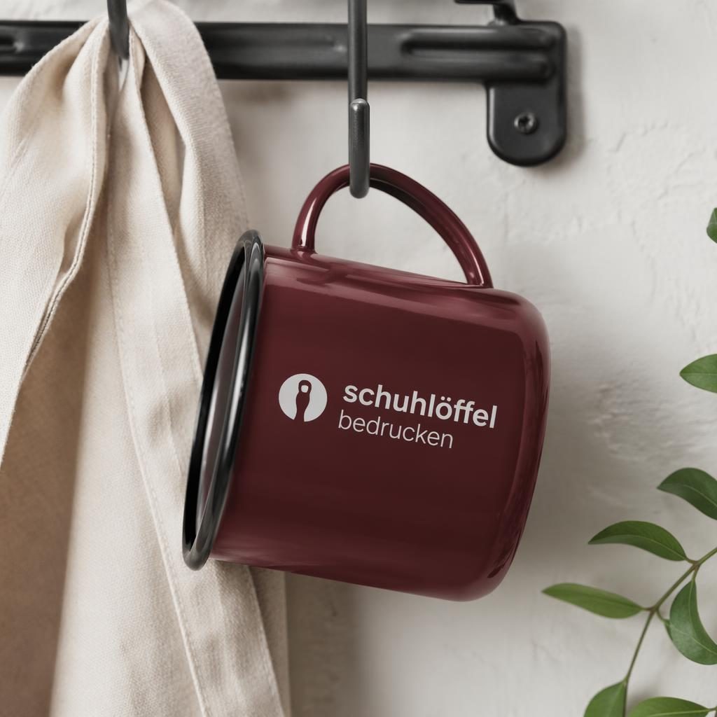Bordeauxfarbene Emaille-Tasse mit umlaufendem Logo, an einem Rack hängend, in schlichter Studioaufnahme