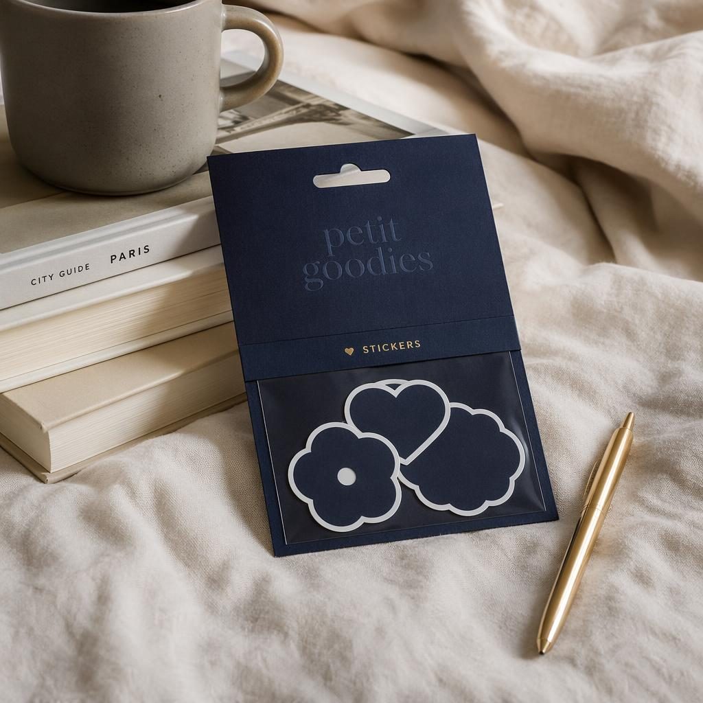Mockup photo-réaliste d’un pack de stickers bleu marine, logo ton sur ton subtil, ambiance maison cosy noire et or.