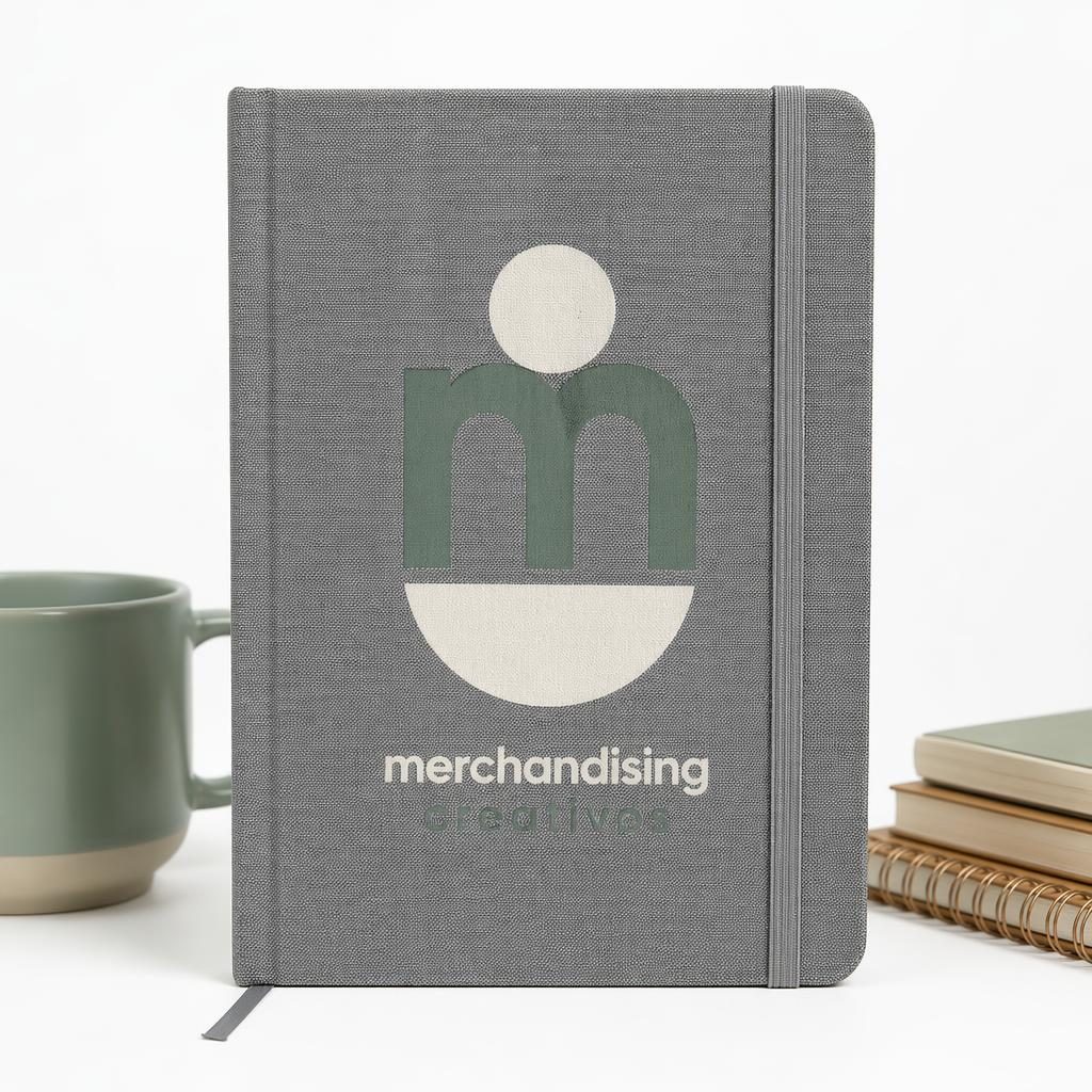 Libreta gris jaspeada con logo merchandising creativos en grande sobre fondo blanco minimalista.
