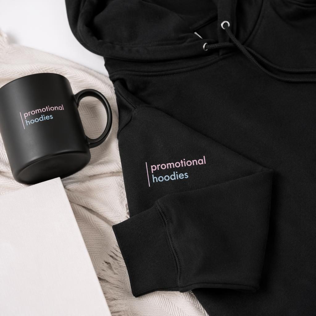 Studio flat lay mockup of a black ceramic mug with generic promotional hoodies logo in a soft pastel palette.