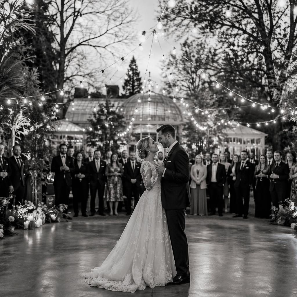 Black and white wedding photo of a groom getting ready in a winter botanical garden, with a first dance under string lights.