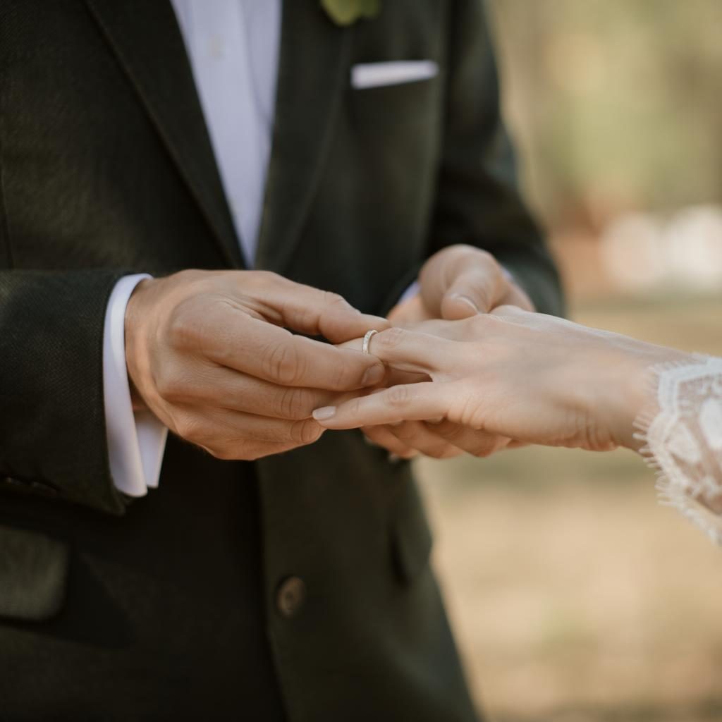 Primer plano de manos durante intercambio de anillos en boda rústica, granero otoñal, luz natural y tonos salvia y blanco.