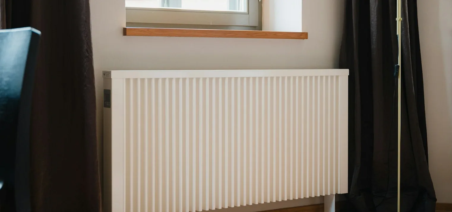 Bílý radiátor pod oknem, který představuje náklady na vytápění.